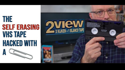 Video thumbnail.
Techmoan holds up a mostly normal looking VHS cassette. There is a "2View" logo displayed on the monitor behind him. The thumbnail's text reads "The self erasing VHS tape hacked with a paperclip". (Instead of the word "paperclip", there is an image of a paperclip used like an emoji)