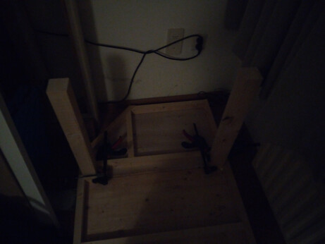 One end of the upside-down table, with two quick-clamps around each table leg, and a corner cut out of the frame design and the tabletop (to make it easier to walk past the table).