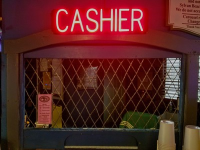 A dingy cashier booth behind a diamond net and a CASHIER sign glowing in red neon above 