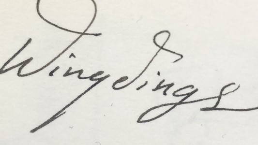 The word “Wingdings” written in cursive, in blank ink on some thick paper. 