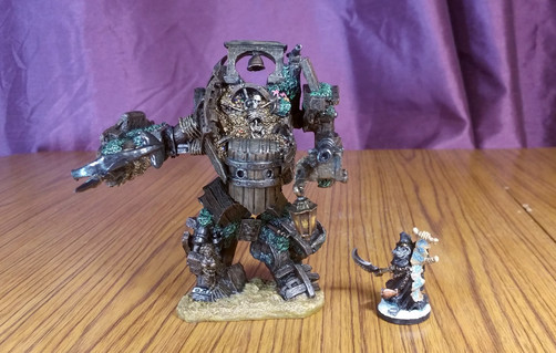 A hulking humanoid construct made of shipwreck bits, stood next to a necromancer holding a scythe & scroll.