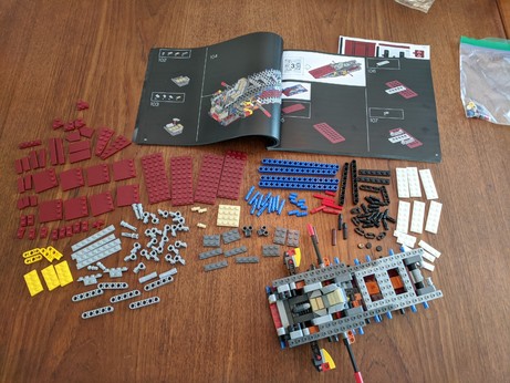 Lots of red LEGO pieces and a smattering of other colors in a large array of loose pieces, somewhat arranged. The model from Stage 2 is also present.