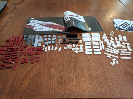 An awful lot of flat LEGO pieces spread out over a table, with lots and lots of red and white bits.