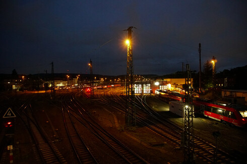 a bunch of train tracks forking off each other, a parking train and some sort of train storage/maintenance building