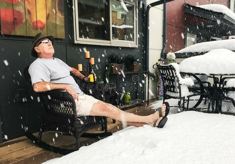 Man drinking beer in summer clothes, while massive piles of snow are around him. 