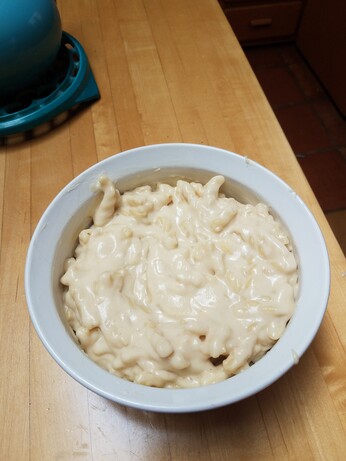 Wooden polished table with a white circular baking dish full of noodles and a thick gooey cheese sauce