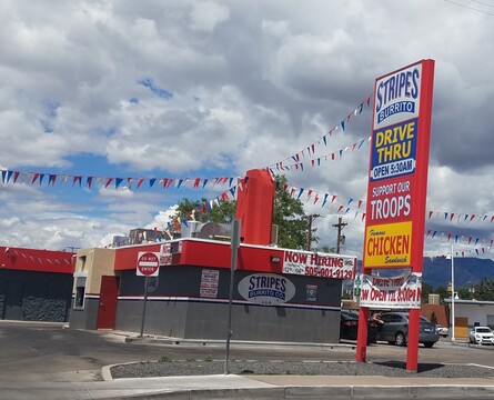Eatery called Stripes Burritos Drive Through. Sign declares "Support our Troops"
Single story grey concrete building with a red flat roof. Sunny day but clouds in sky