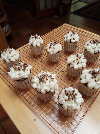 10 cupcakes on a brass cooling rack with cream cheese frosting and a pecan garnish