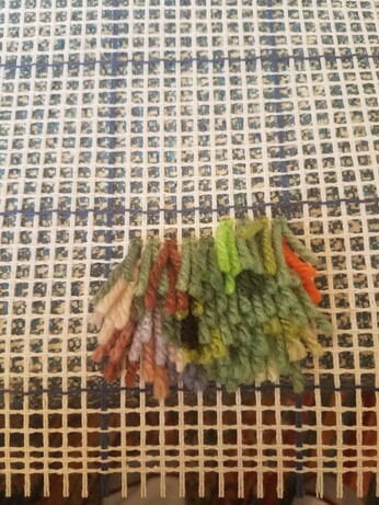 Blotches of green, orange, ans brown yarn tied to a lattice. No image yet
