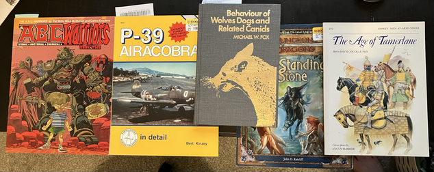 From left to right; a compendium of old b/w British comics, a Squadron guide to the P-39, a scholarly and possibly outdated hardcover about canine behaviors, a 3e module, and an Osprey book about Timurid armies.