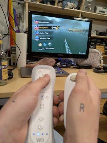 wiimotes in hands tattooed L and R, with Mario Kart World running on a screen behind them